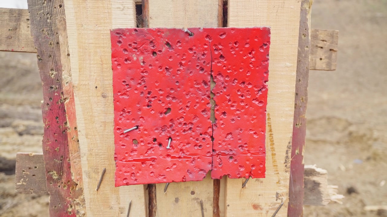 Bersaglio rosso crivellato di fori di proiettile con danni visibili da ripetute sessioni di tiro.