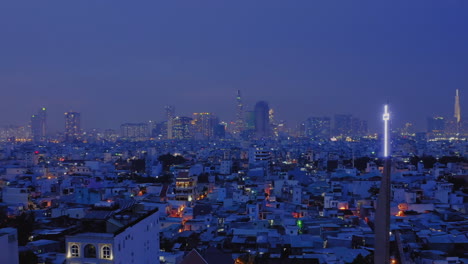 4k-Drohnenaufnahmen,-Die-Nachts-Ein-Weißes-Neonfarbenes-Christliches-Kreuz-Auf-Einem-Kirchturm-Umkreisen-Und-Die-Lichter-Der-Stadtlandschaft-Und-Der-Skyline-Der-Stadt-Enthüllen-Und-Das-Christentum-In-Den-Mittelpunkt-Stellen