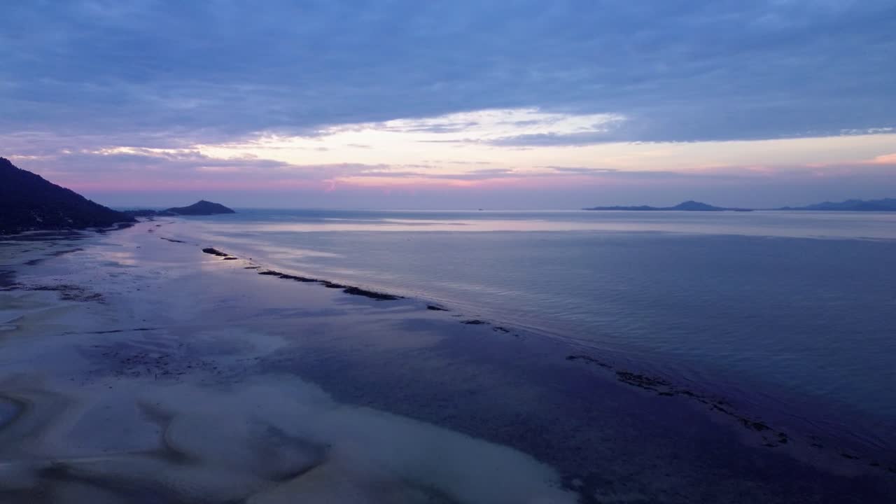 Beautiful aerial drone footage of sunrise over Koh Phangan, Thailand, featuring a pink horizon, calm sea, tropical coastline, and scenic island landscape in morning light