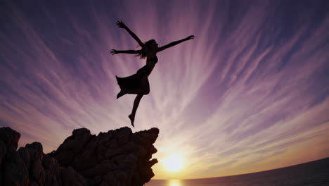 dynamic silhouette of a woman leaping from a cliff at sunset by the ocean