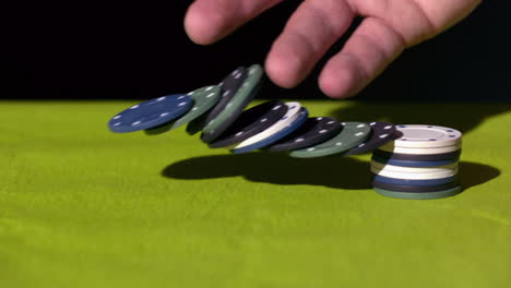 hand knocking over stack of casino chips on green surface