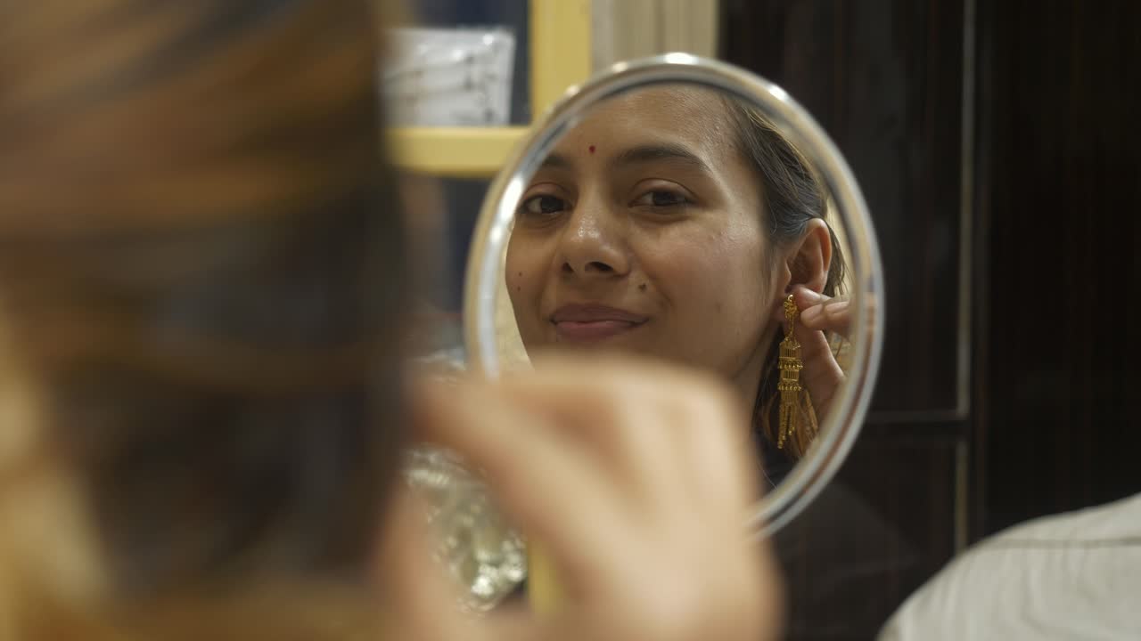 Giovane e bella donna asiatica che indossa orecchini d'oro 18k certificati HUID di design, si guarda allo specchio e sorride.