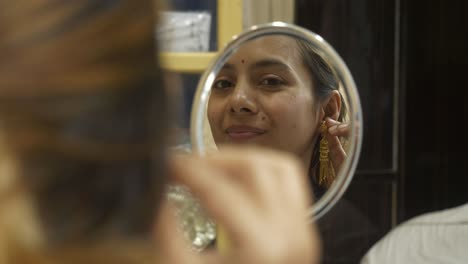 young beautiful asian woman wearing designer 18k huid certified gold earrings, looking at mirror and smiling