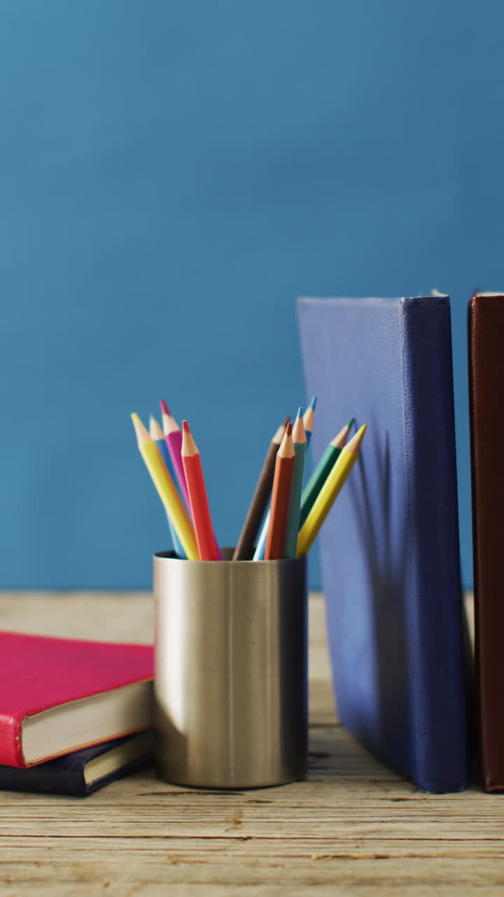 video vertical de un contenedor con lápices de colores y libros sobre fondo azul