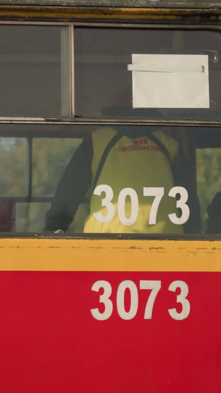 red yellow tram window showing worker inside. Closeup of tram side numbered , highvisibility jacket glimpsed through tinted pane, worn paint and metal trim, decal and adhesive residue on glass
