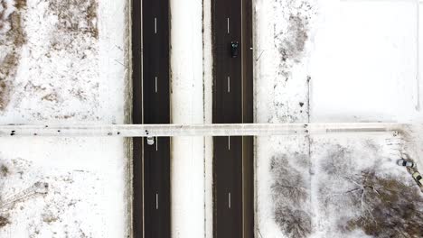 People-walking-over-A1-highway-on-wooden-pedestrian-bridge-covered-in-snow,-top-down-aerial-view