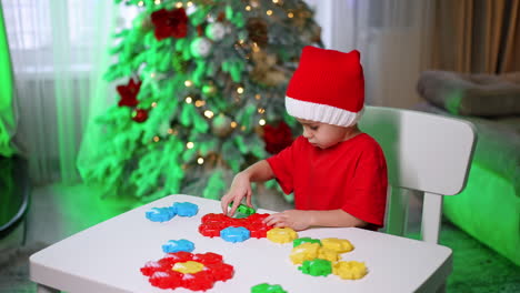 child playing with colorful blocks. a young child in a red outfit plays with colorful blocks at a white table, festive decorations around them