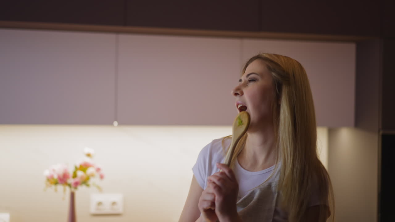 la mujer se divierte bailando y cantando en la cuchara en la cocina