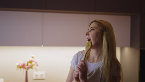 la mujer se divierte bailando y cantando en la cuchara en la cocina