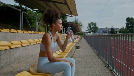 woman resting and drinking water at a stadium