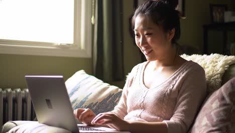 a young woman engaged in enjoyable online activity while relaxing on a cozy couch, smiling and using her laptop in a comforting home environment