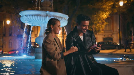 parejas alegres disfrutando de una cita en la ciudad de la noche. pareja sonriente viendo móvil