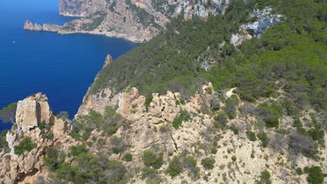 group of tourists hiking on a rocky cliff in ibiza, spain, enjoying the breathtaking view of the mediterranean sea. great aerial view flight panorama orbit drone