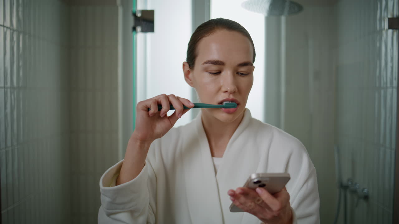 Attractive woman cleaning teeth in morning. Closeup girl browsing mobile phone