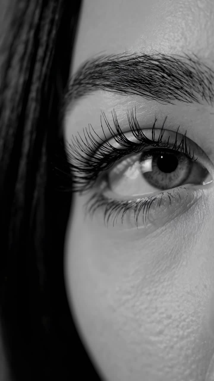Close-up, black and white video frame of a woman's eye, capturing intricate details and textures
