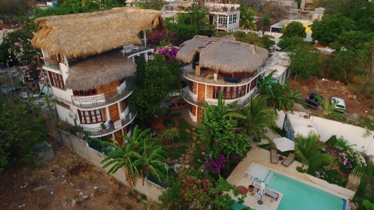 Circling around a chic little boutique resort with a swimming pool and natural material roof alongside tropical landscaping in the tourist town of Puerto Escondido in Mexico