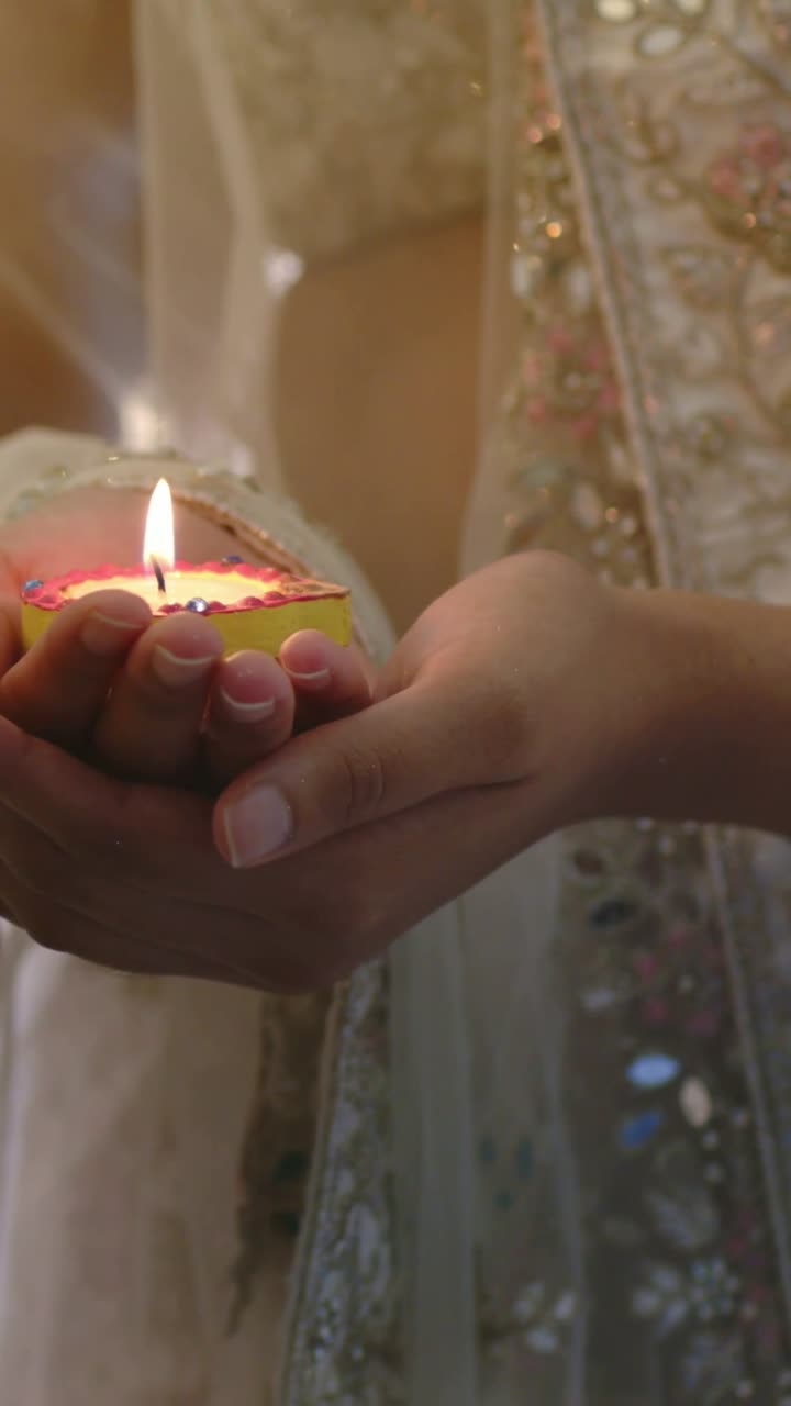 Vertical video: Prayer starting, woman in embroidered sari holding clay diya steady in warm room