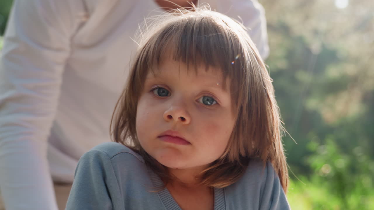 Close up of young girl sitting up with sleepy expression under warm sunlight, eyes half open showing exhaustion and tenderness, calm atmosphere surrounded by soft natural light