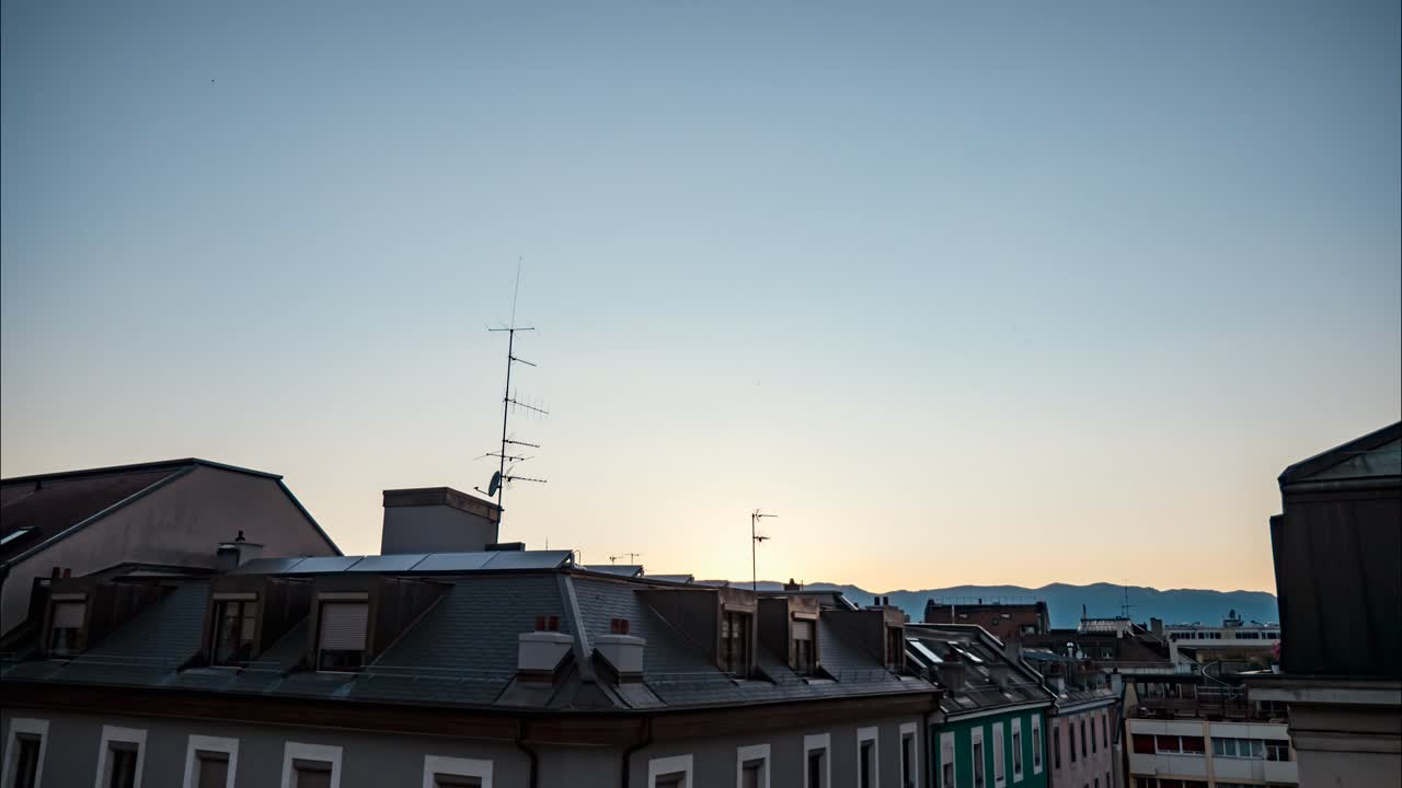 Bright white sun and beam above buildings in blue sky with clouds by distant mountain range at sunset, time lapse day to night