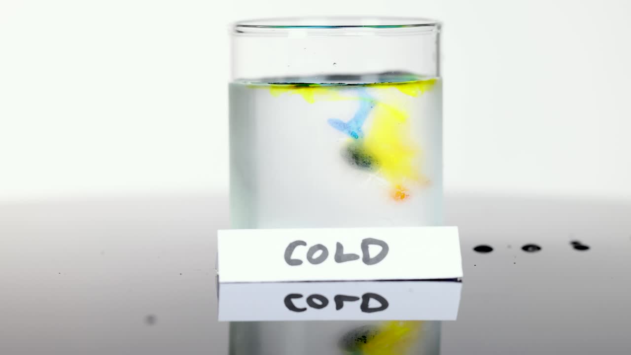 Colored drops disperse slowly in clear cold water, captured in bright, static, high-key studio lighting