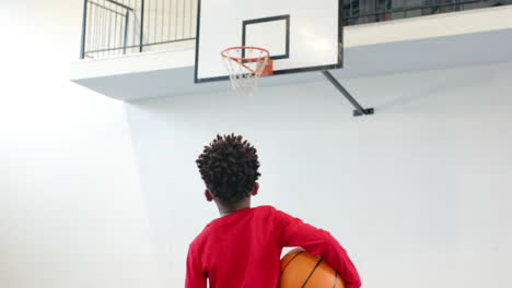 holding basketball, african american boy focusing on hoop in school gymnasium, practicing shot