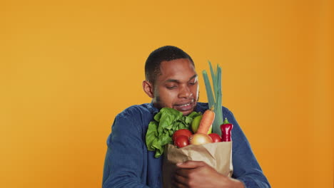 joven luchando para llevar una bolsa de papel llena de frutas y verduras biológicas frescas
