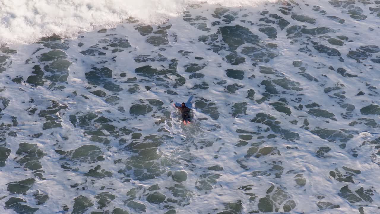 A surfer paddles through rough ocean waves on the Gold Coast, capturing dynamic movement and natural beauty