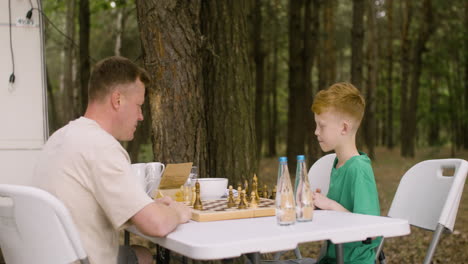 padre e hijo jugando al ajedrez en el campamento en el bosque