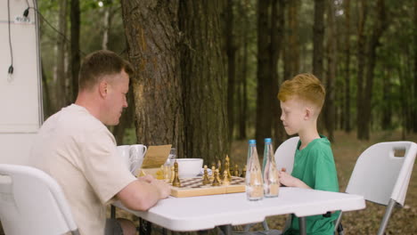 vater und sohn spielen schach auf dem campingplatz im wald