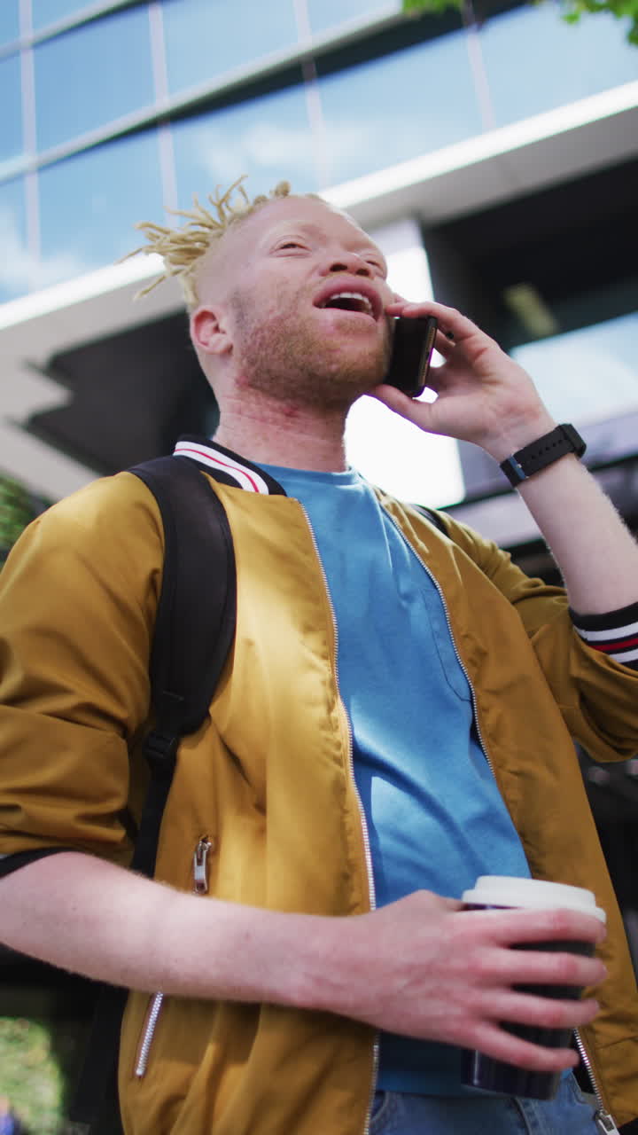 Video verticale di uomo albino con i dreadlock che usa lo smartphone in piedi in una strada cittadina.