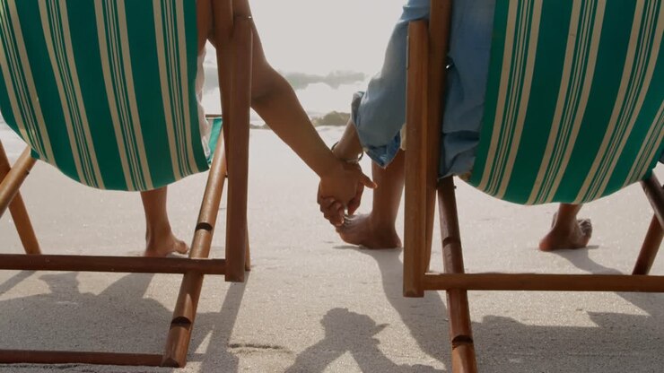 Vista posteriore di coppia afroamericana che si rilassa mano nella mano su una sdraio sulla spiaggia 4k