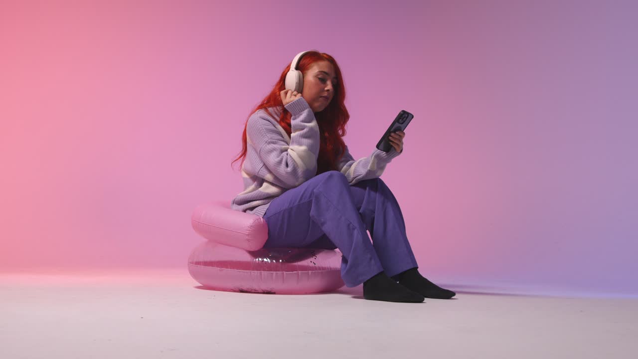 fotografía de estudio de una mujer joven de la generación z con auriculares transmitiendo música al teléfono móvil