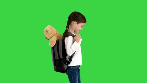 una niña linda caminando a la escuela con un oso de peluche sobresaliendo de su mochila en una pantalla verde, llave de croma