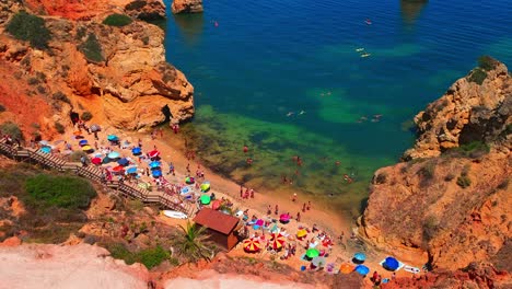 Scenic-view-from-the-coastline-of-Praia-do-Camilo,-Lagos,-Portugal,-with-umbrellas-and-a-bustling-crowd-of-people