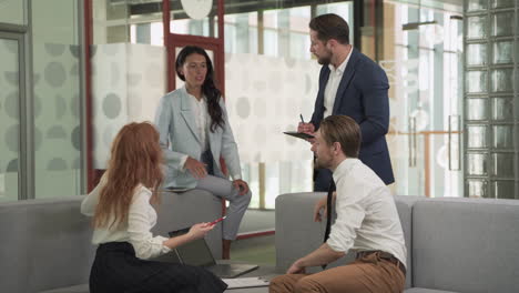 a business working group consisting of two women and two men have a relaxed meeting in the armchairs in the common area of the offices 2