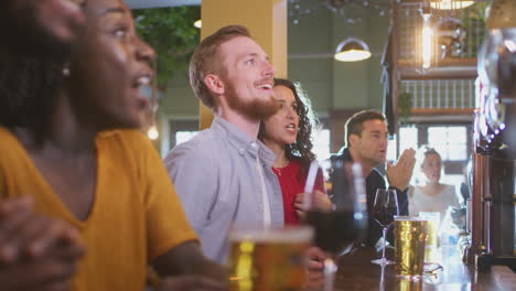 group of excited customers in sports bar watching sporting event on television