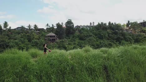 slow-motion shooting of a beautiful girl running down the path in a rice field on a background of palm jungle