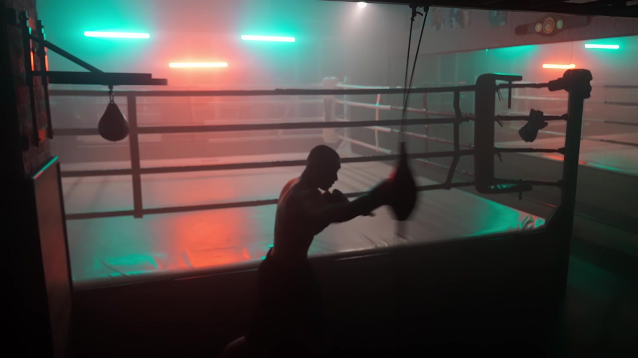Silhuet af mandlig bokser, der træner med en speedbag i et mørkt fitnesscenter.