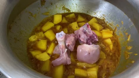 raw chicken pieces being added to bubbling curry sauce with diced potatoes in large pot