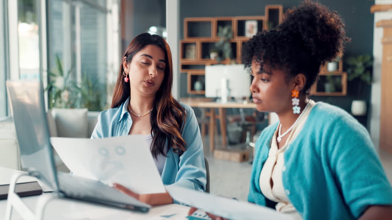 Due donne d'affari discutono documenti e laptop in un ufficio moderno