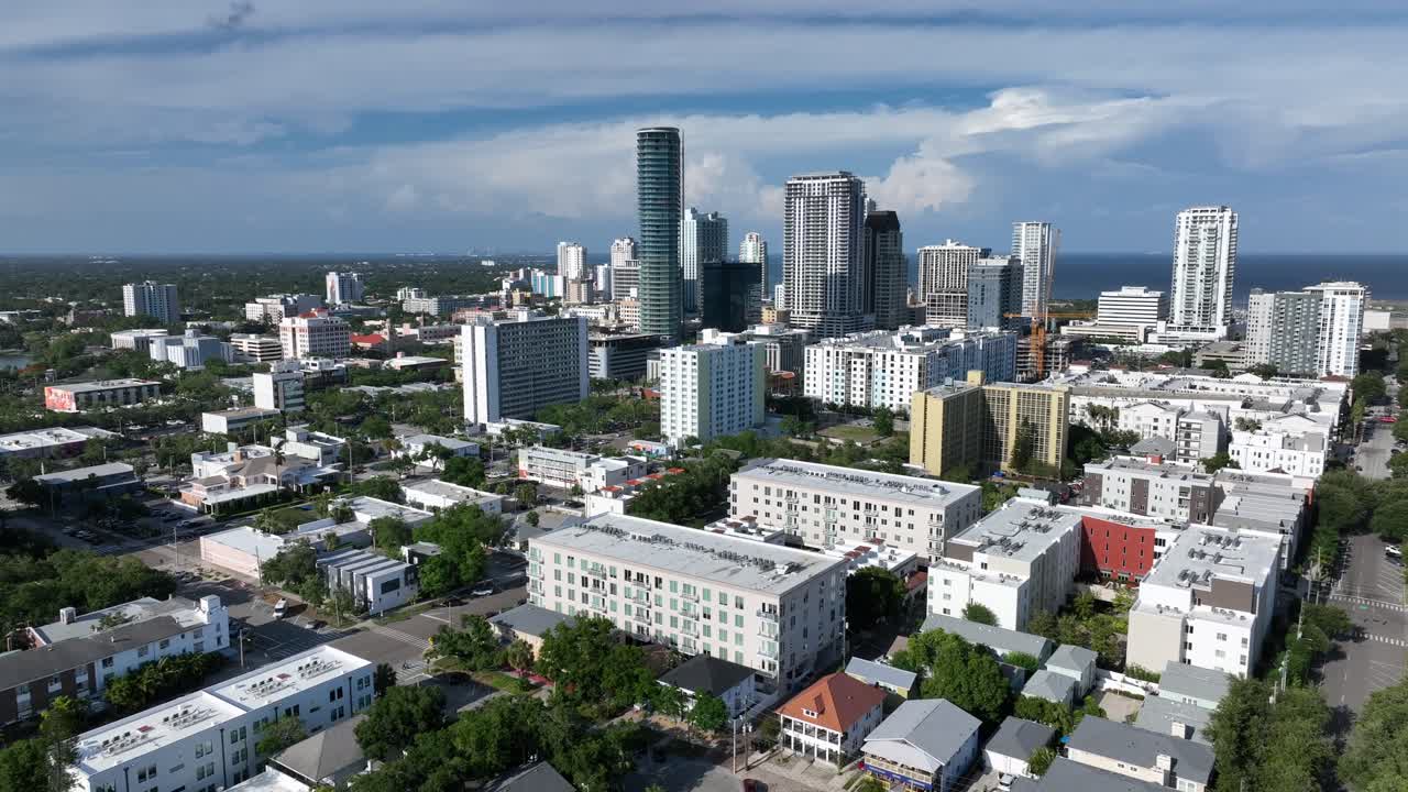 Modern skyline and skyscraper of St. Petersburg Downtown in Florida. Roofing flight over apartment houses and homes in luxury district. Gulf water in distance. Aerial backwards wide shot.