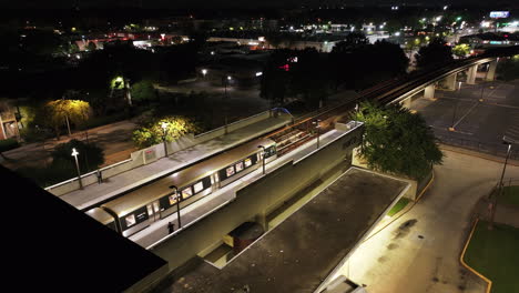 Toma-Aérea-Nocturna-Del-Tren-Saliendo-De-La-Estación-De-Metro-Por-La-Noche