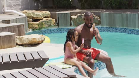 happy african american father and daughter eating ice creams at swimming pool