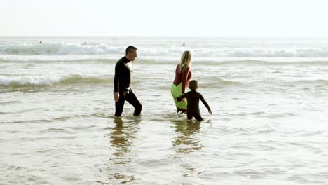 family in wetsuits walking in sea