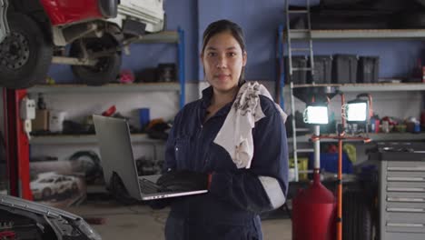 retrato de una mecánica usando una computadora portátil y sonriendo en una estación de servicio de automóviles