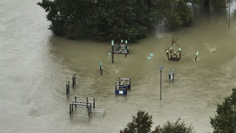 aerial view of flooded playground with rising waters from the river submerging play equipment and nearby trees, demonstrating the impact of severe flooding