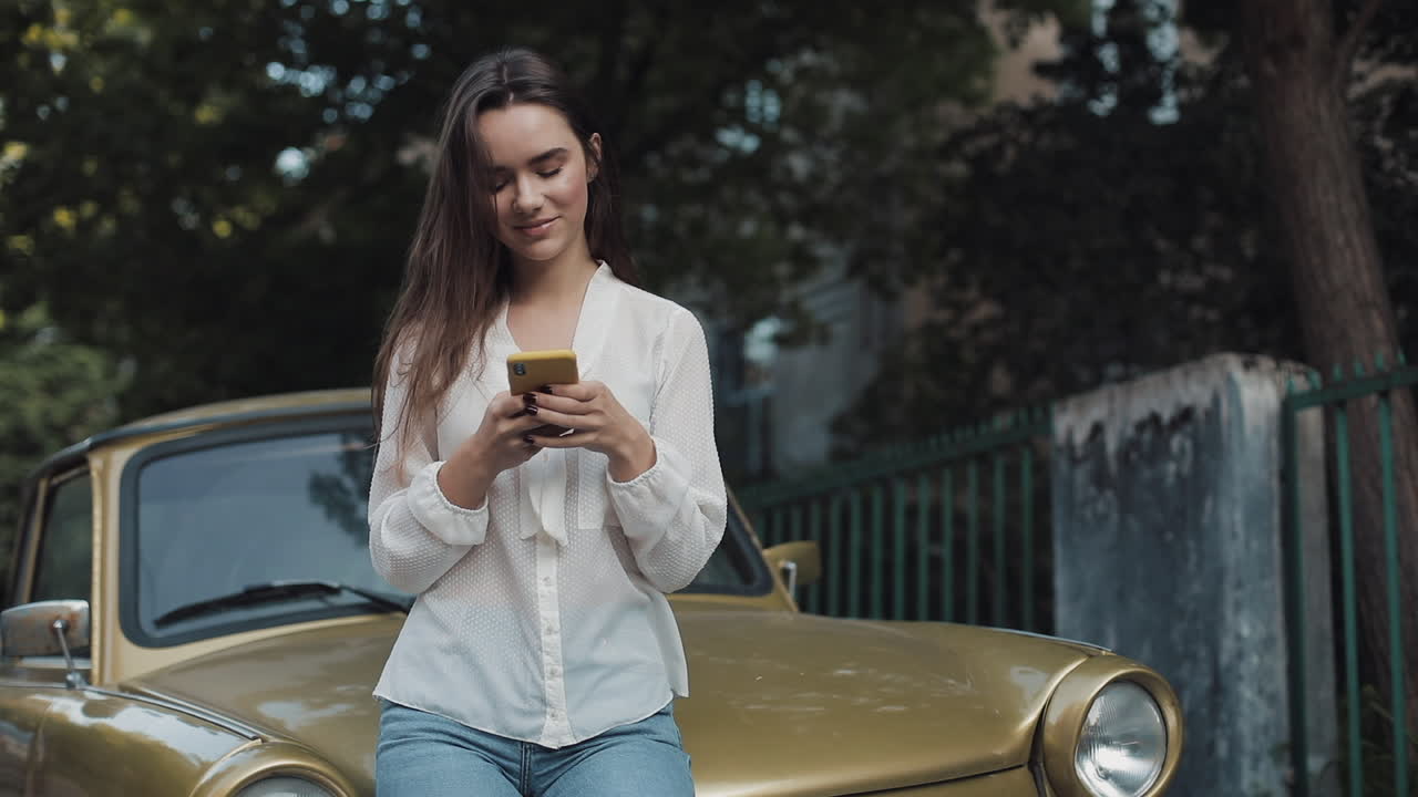 Woman with mobile phone by classic car