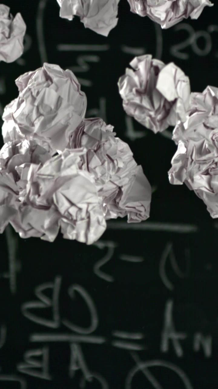 White Crumpled Paper Falling in Front of a Chalkboard with Equations
