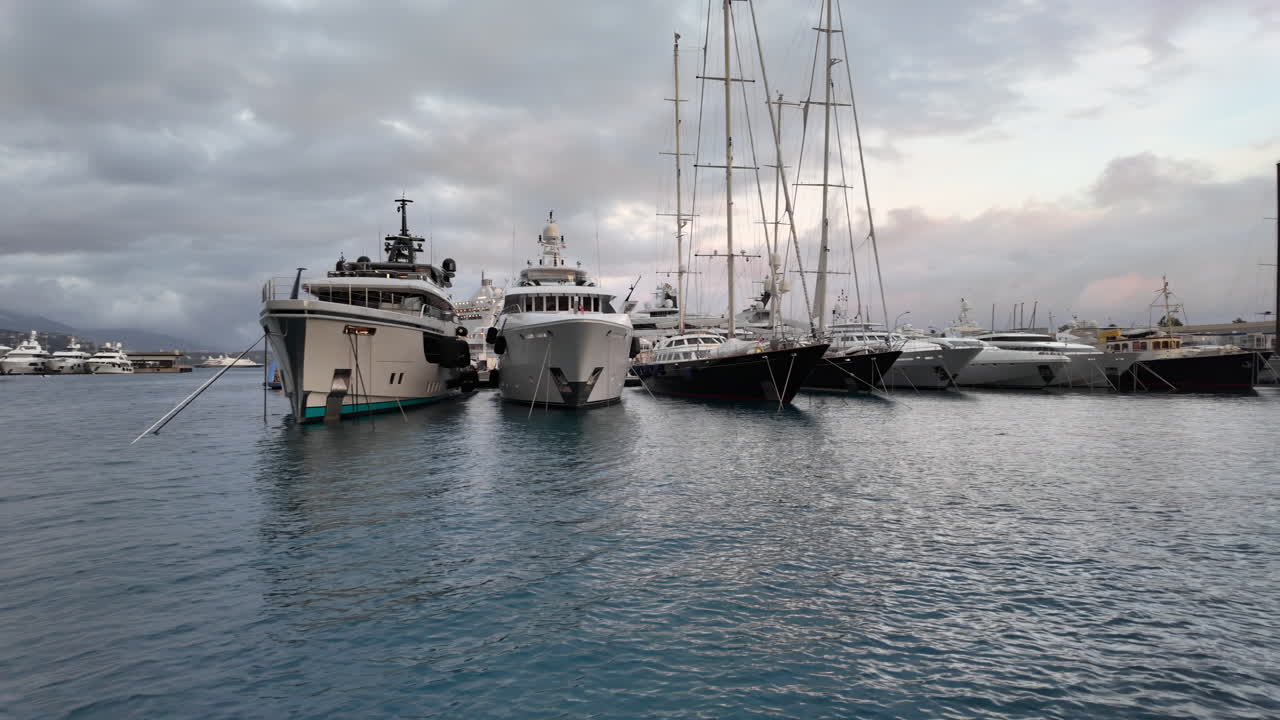 La Condamine, Monaco - July 4, 2025: Row of sleek luxury yachts, docked in Port Hercules with the Monaco cityscape and misty hills in the background