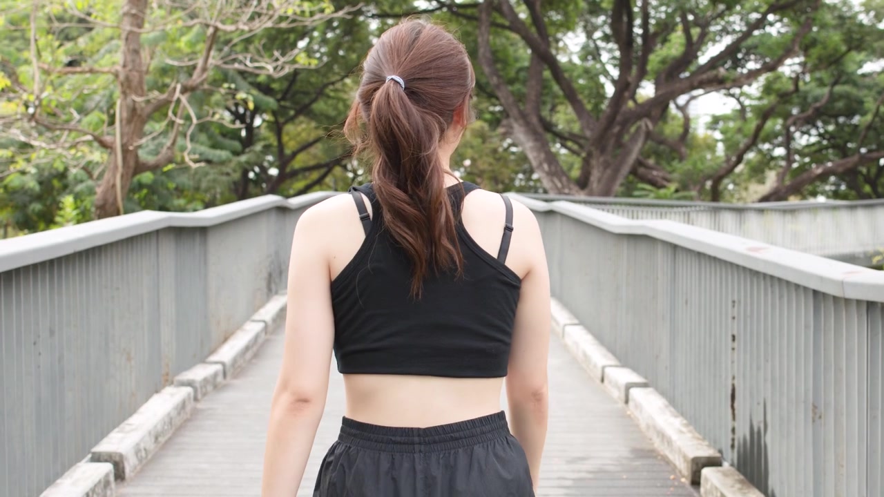A woman in black activewear jogs away from the camera on a park bridge